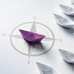 Purple paper boat on a compass among white boats, representing independent Forex Treasury advice and business-led decision-making.